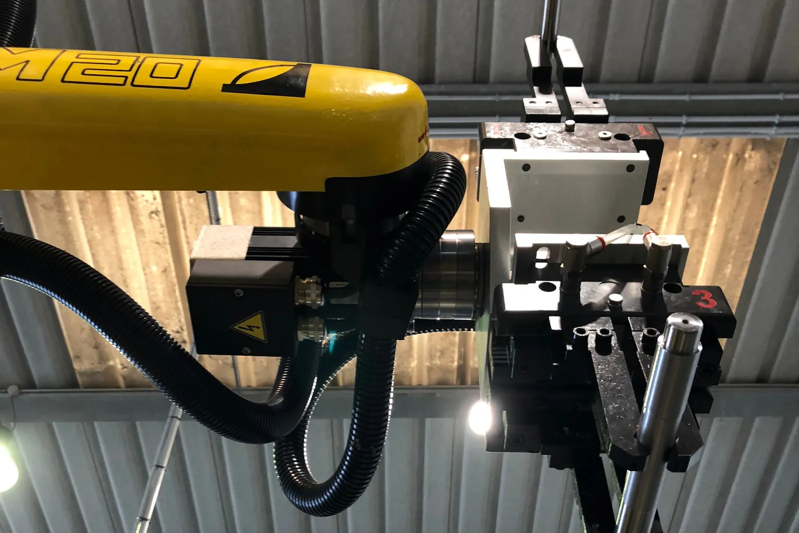 Yellow manipulator arm with a gripper holding a steel shank